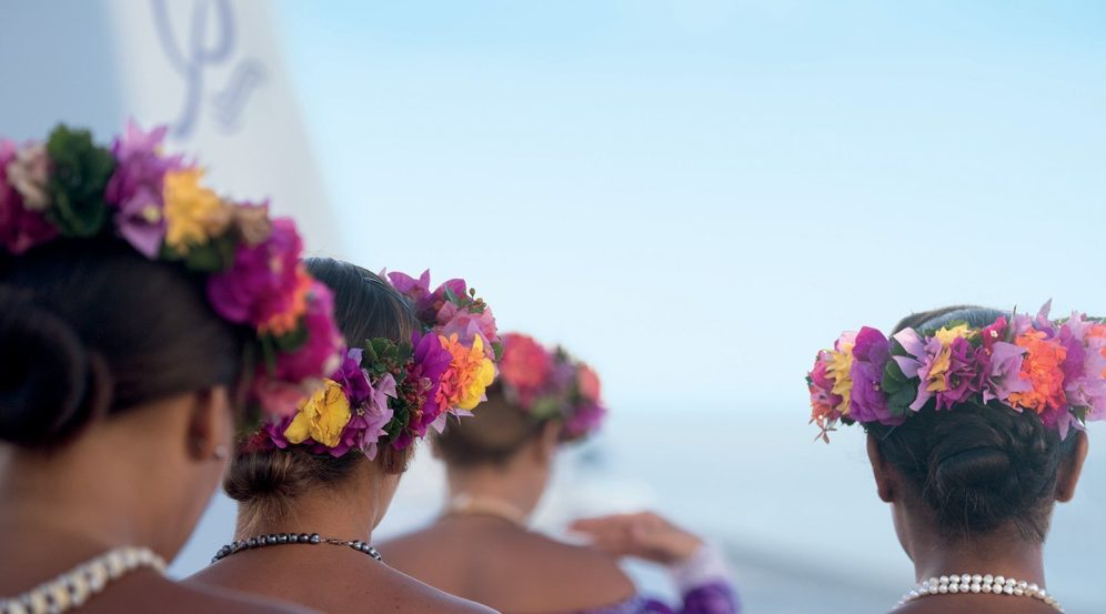 Four women wearing flower crowns walking away from the camera. Taller image.